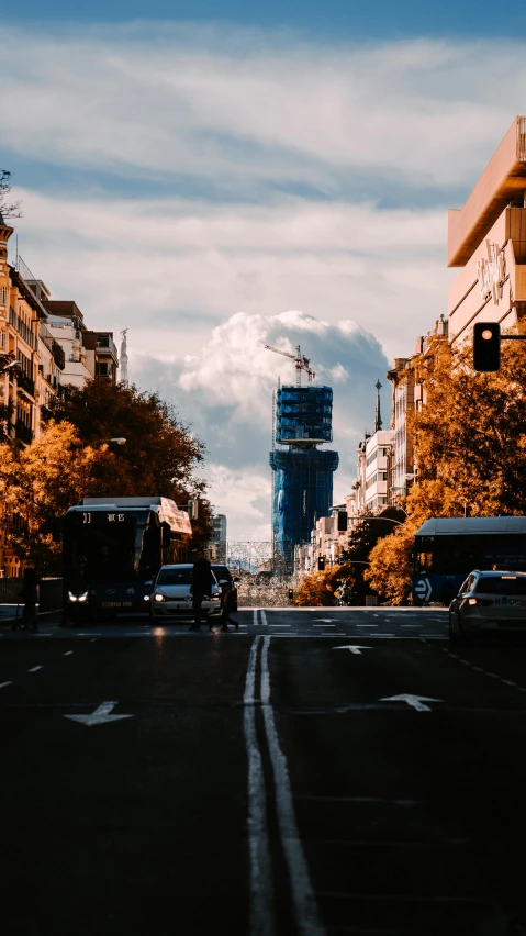 an empty street with two buses passing on the opposite side and two trees in the background