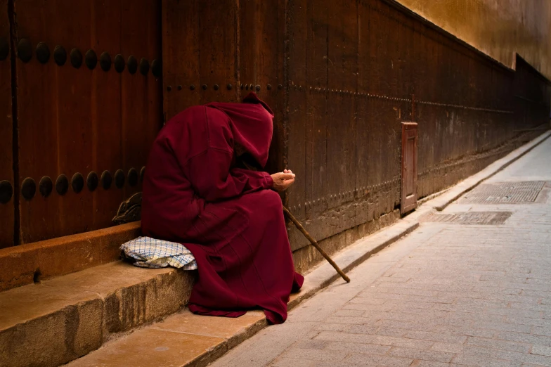 a person in a hooded hood leaning against a wall with his head up