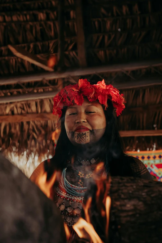 a woman dressed in a flower crown stands in front of fire