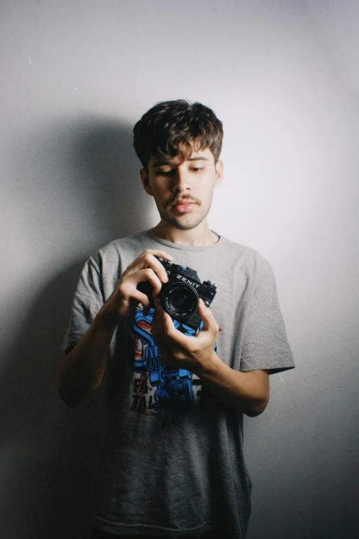 a young man is holding a camera by a wall