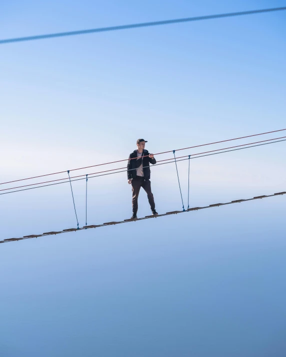 a man on a wire suspended bridge walking on it