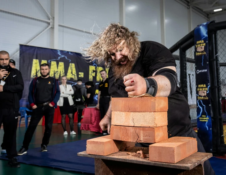 a man in black shirt with long hair and beard,  bricks into pieces