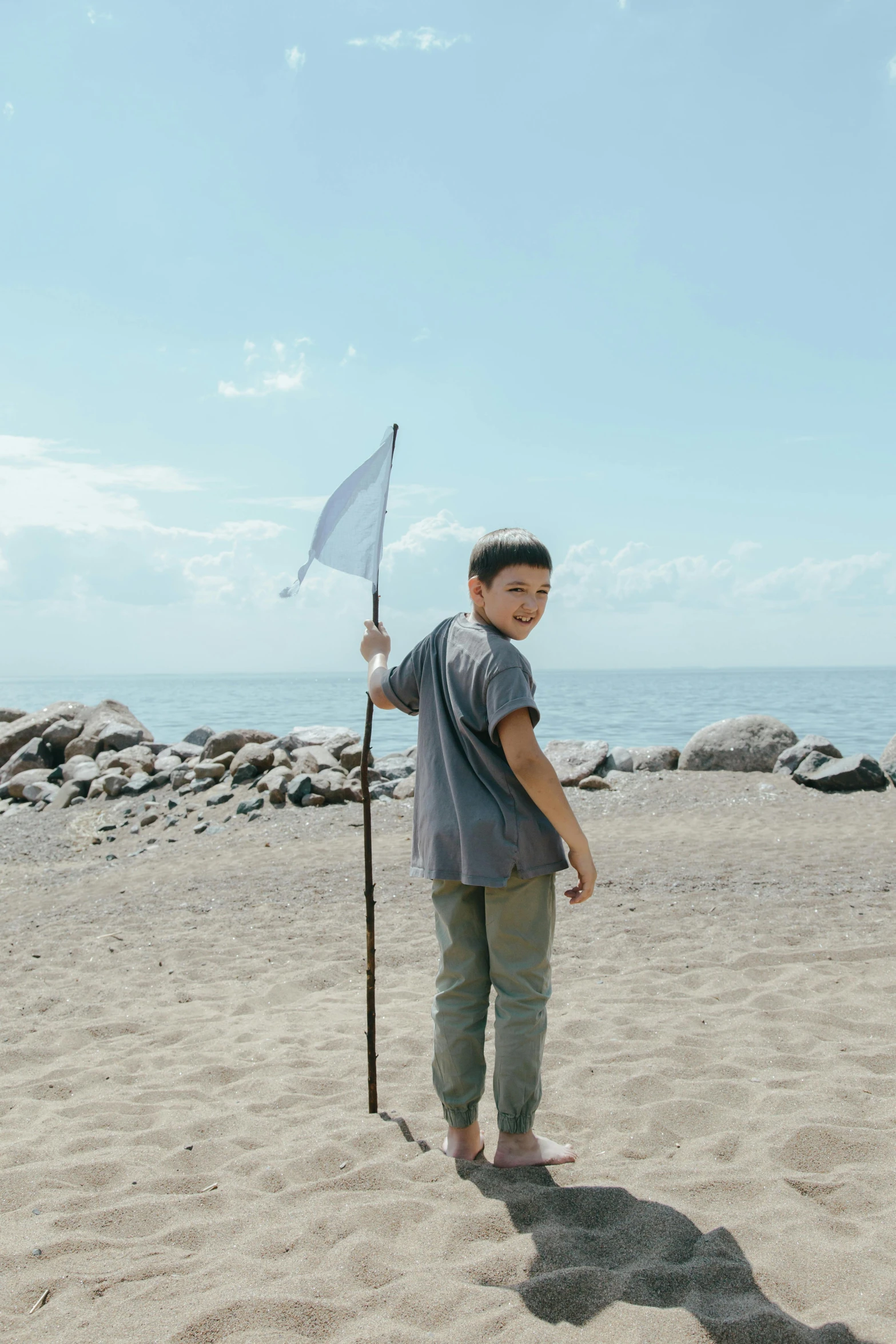 a boy standing in the sand while holding an umbrella