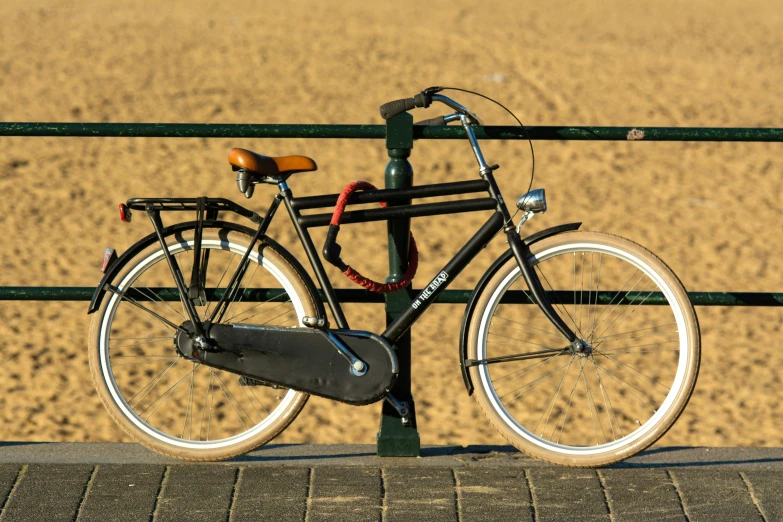 a bicycle leaning up against a fence in front of a sandy area