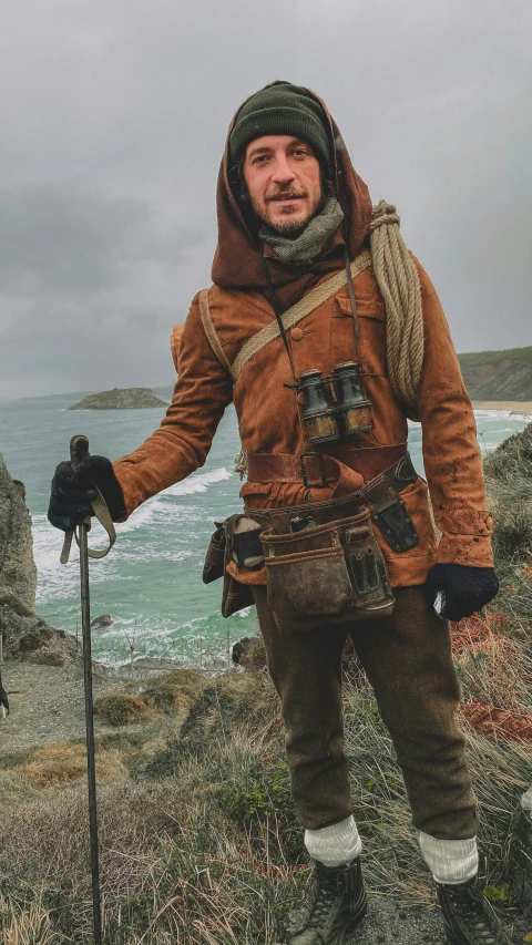 a man with a jacket and scarf standing in the grass near the ocean