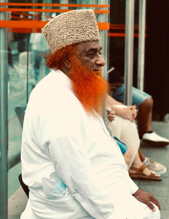 a man with orange hair sitting next to a metal fence