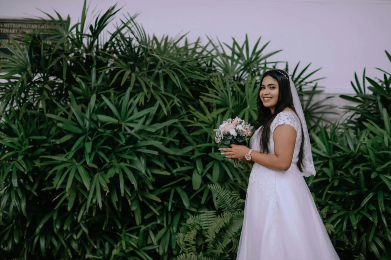 a bride is holding her bouquet while standing next to some plants