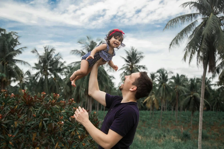 man holding up a child in the air near palm trees