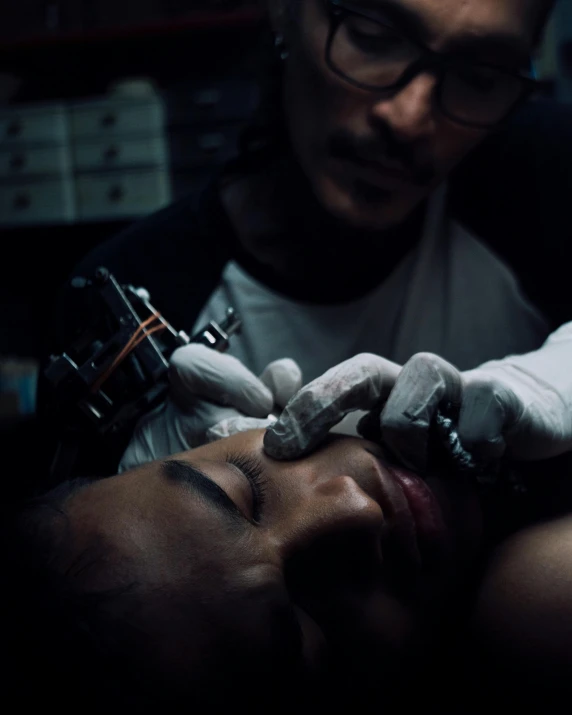 a person in gloves and glasses examines another persons face