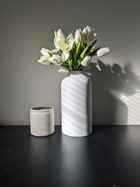 white flowers are in a ceramic vase sitting next to a light that casts a shadow