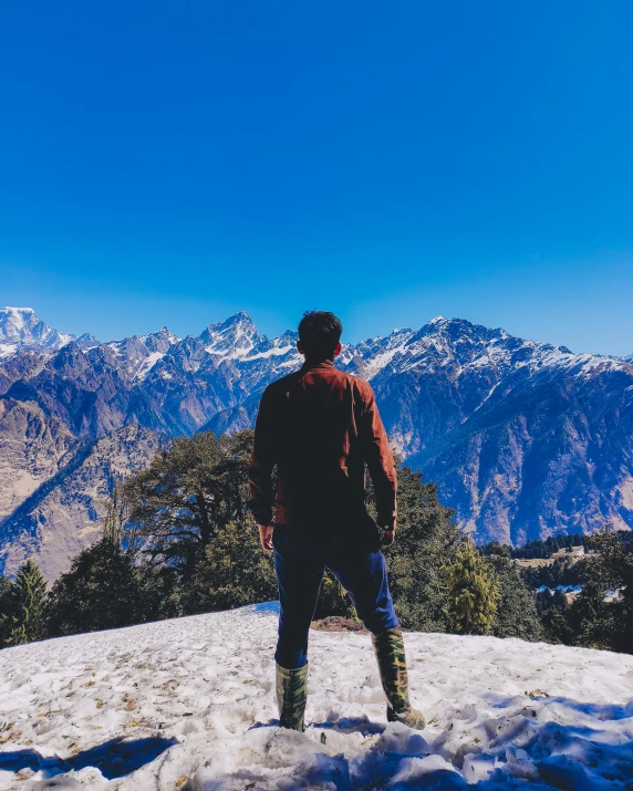 a man stands at the top of a snowy mountain looking out over snow covered mountains