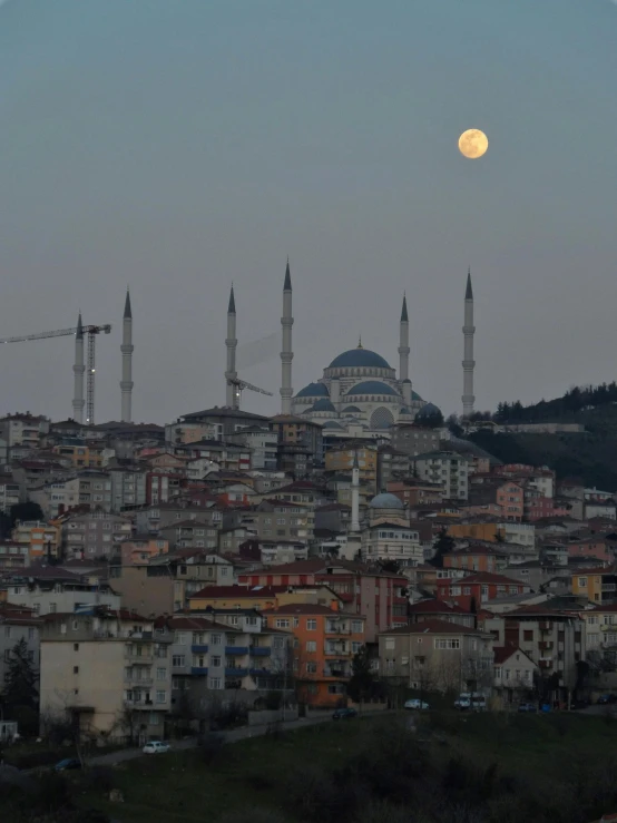 a full moon rises over a city in the distance