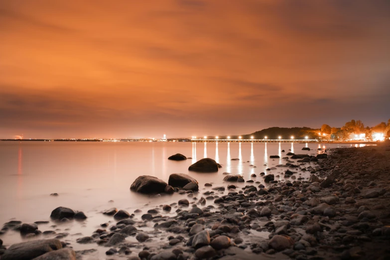 a red and black sky above the water and rocks