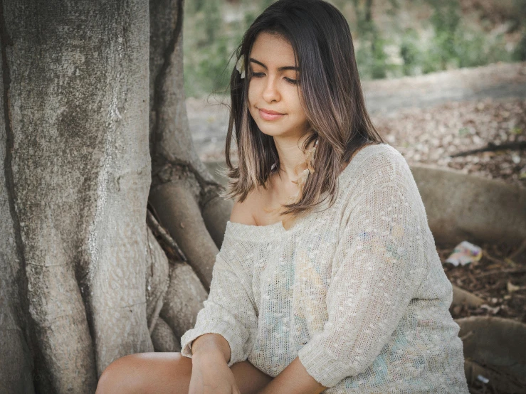 a girl sits near the edge of a tree and stares off