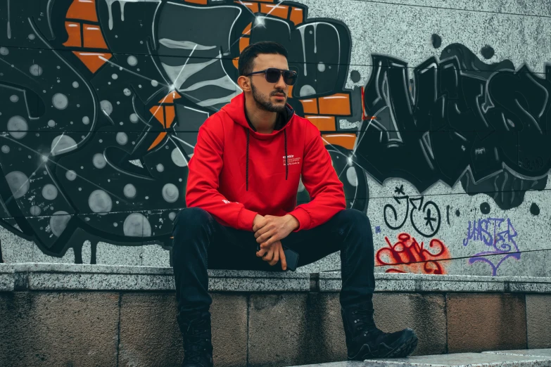 the man is sitting against the wall near a graffiti wall