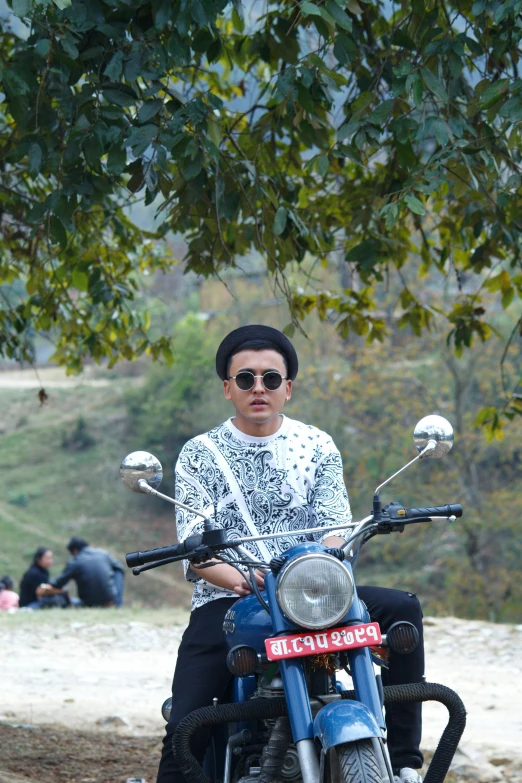 a man sitting on a blue motorcycle next to trees