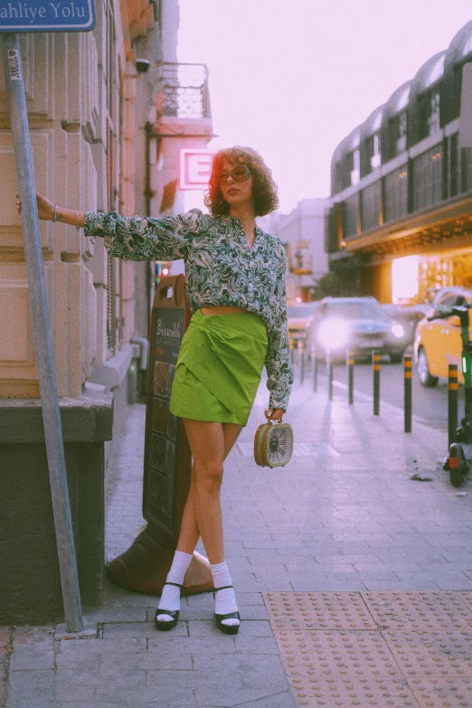 the woman wearing green dress is posing next to a street sign