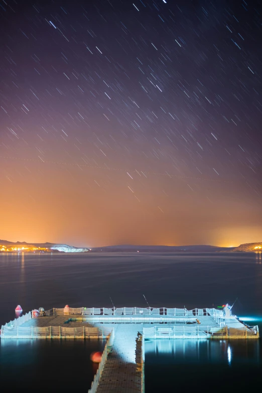 a dock in the middle of the ocean with a sky full of stars above