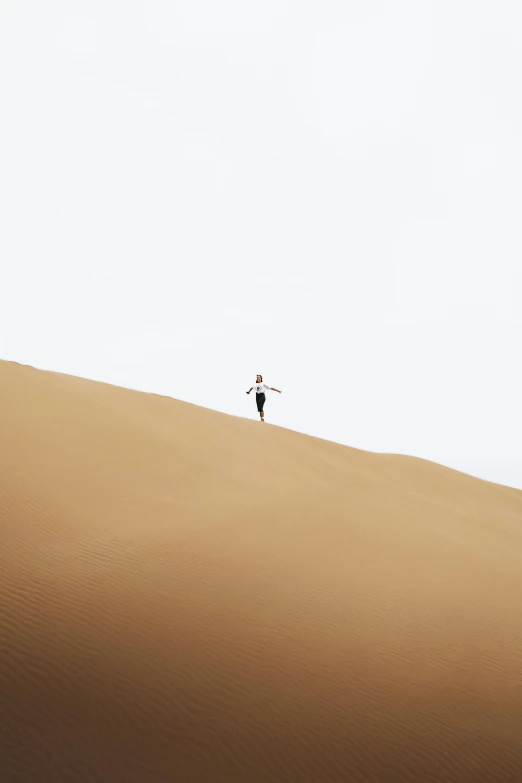 a man standing on the top of a large, sandy hill