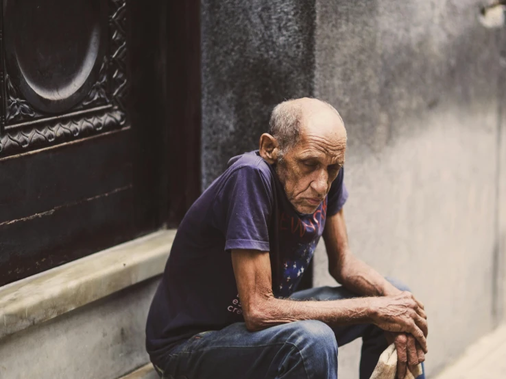 a elderly man is sitting on the ledge outside of a building