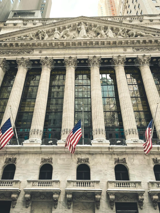 the new york stock exchange building and flags are waving