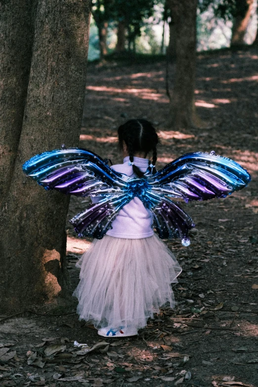 a  in a fairy costume stands behind a tree