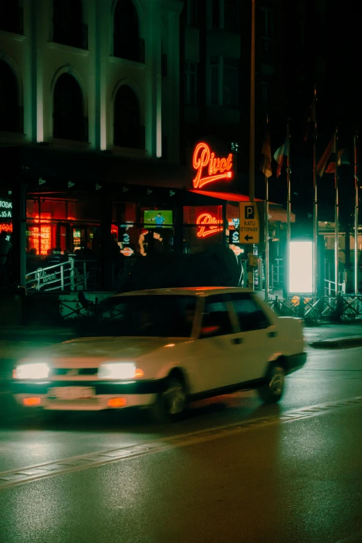 a white car driving past a restaurant at night