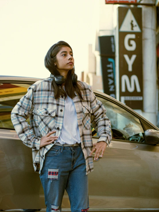 a young woman wearing jeans and a checkered jacket is standing in front of a car