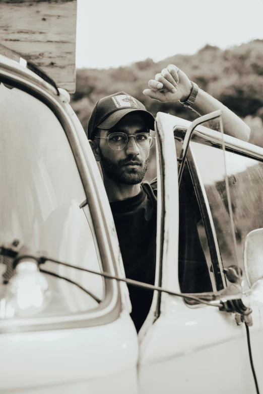 a young man sits in the drivers seat of a truck while leaning his head out the window