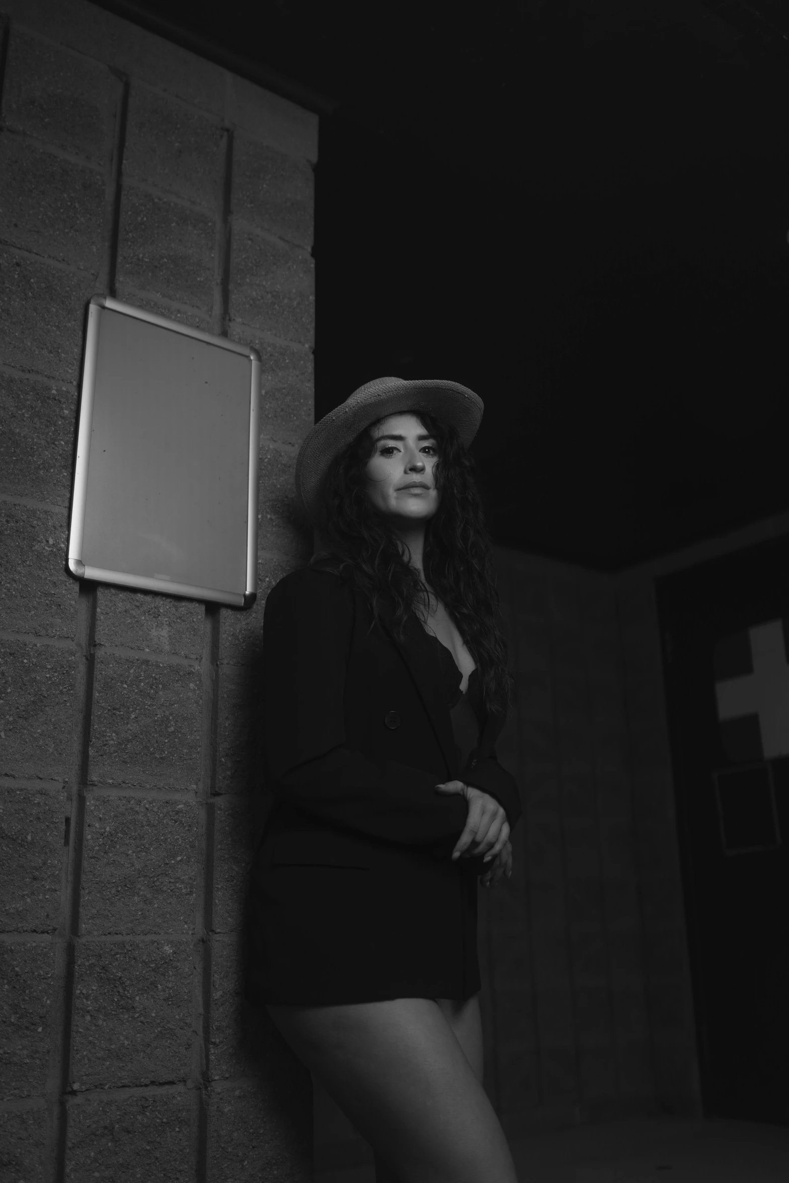 woman in short shorts and a fedora leans against a wall