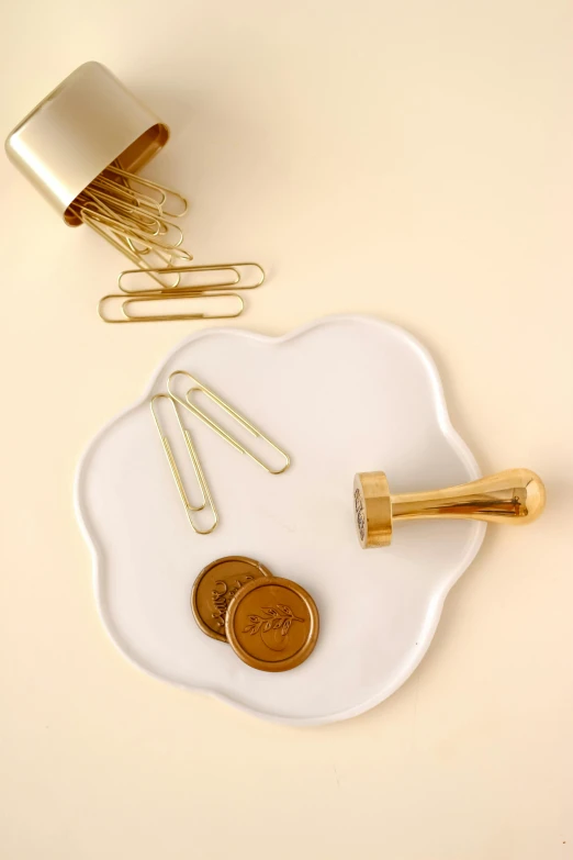 some paper clips, money and a roll of gold hair pins are on a plate