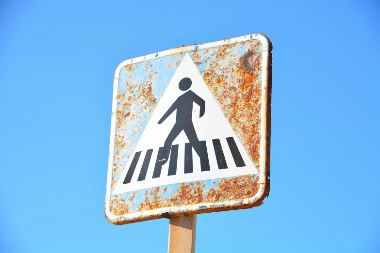 a rusty pedestrian crossing sign in front of a blue sky