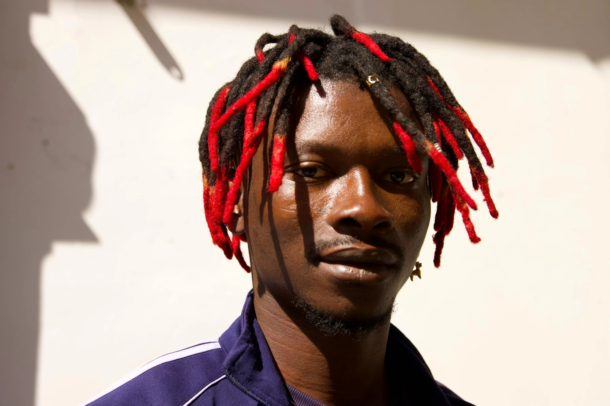 a man with long red dreadlocks standing against a white wall