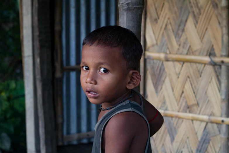 a  in a vest standing near a bamboo hut