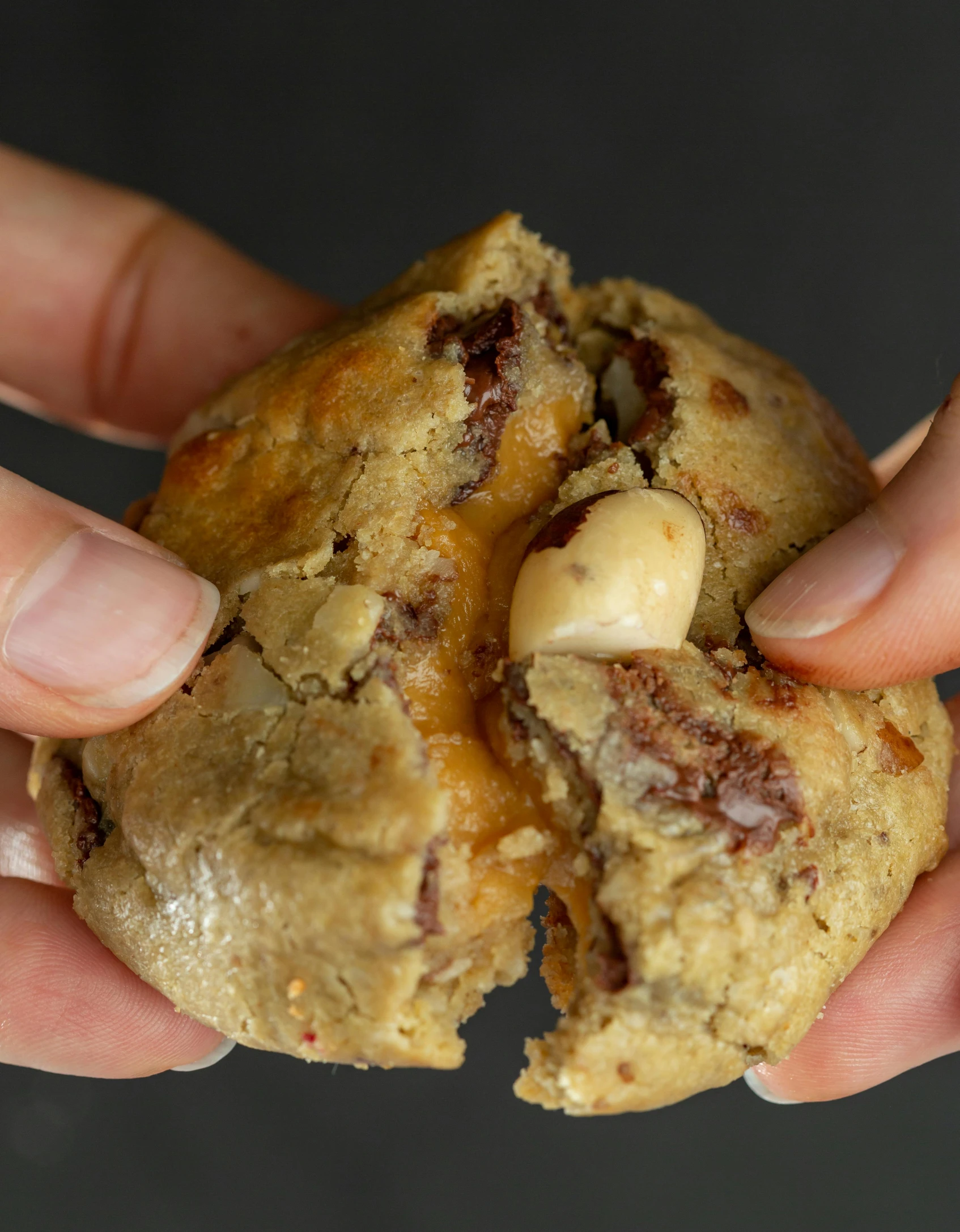 two hands holding a chocolate chip doughnut that is broken open