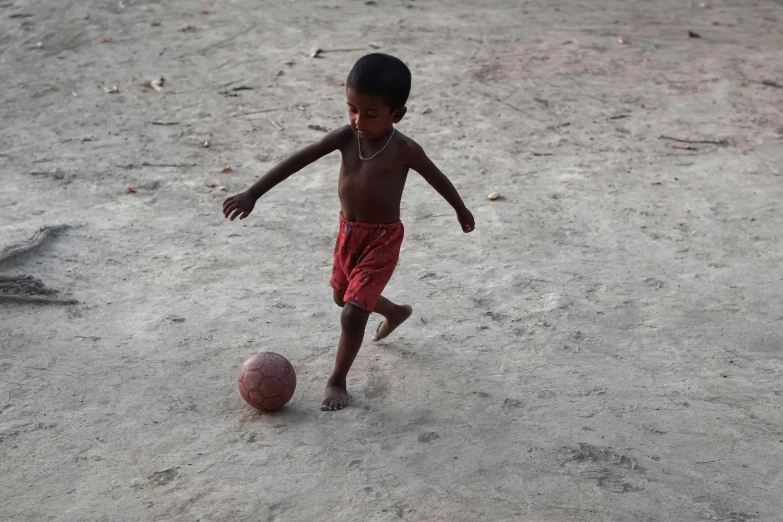 a little boy standing on the beach next to a ball