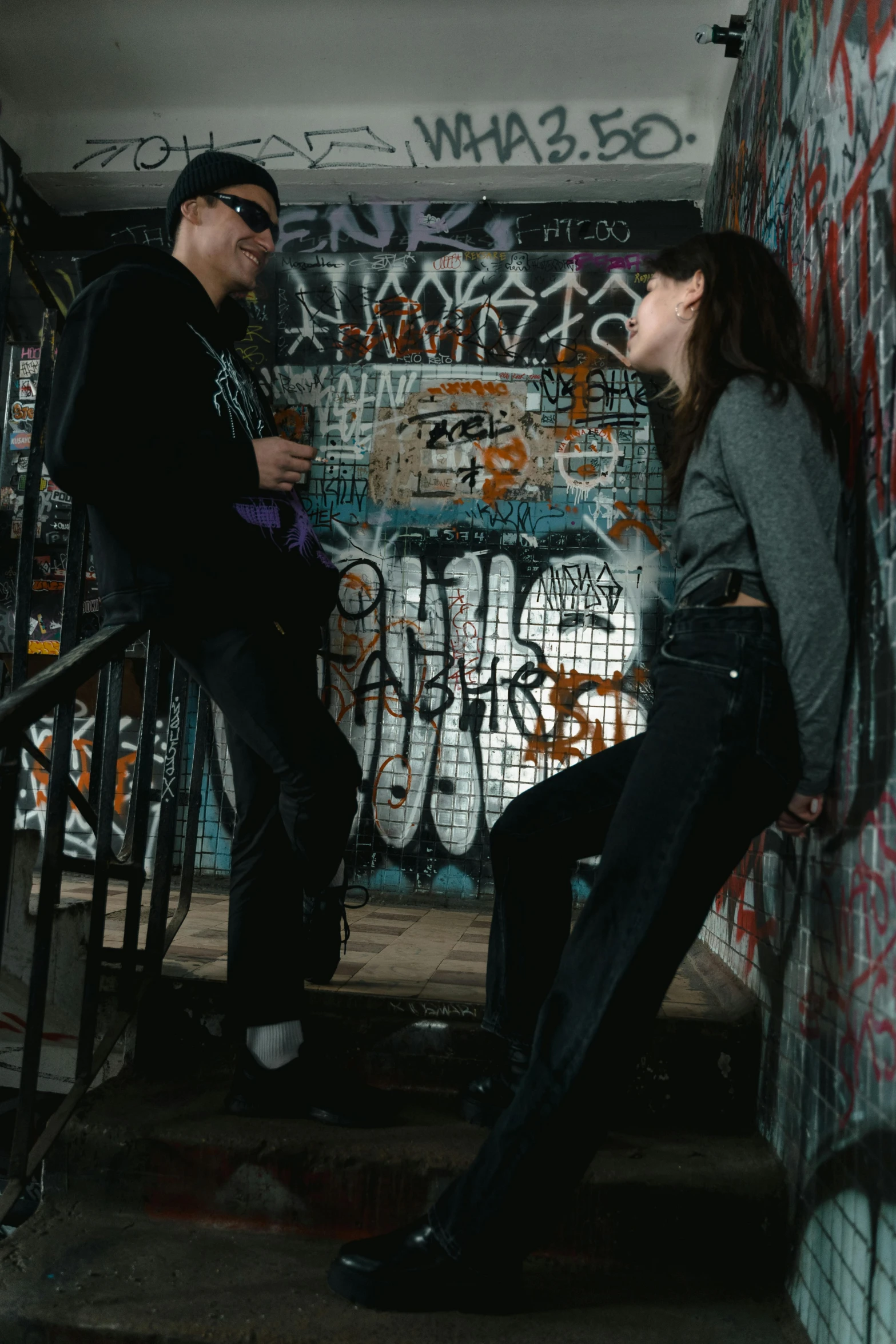 two people standing near an alleyway with graffiti all over it