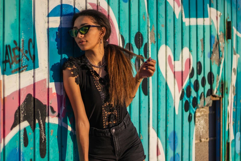 a woman leaning against a wall holding her hair in one hand and a skateboard in the other