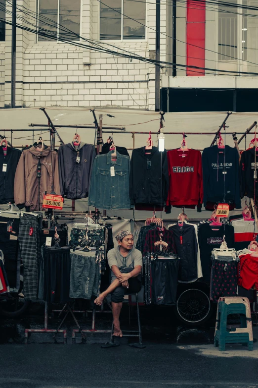 an old man sitting on a chair behind some clothes