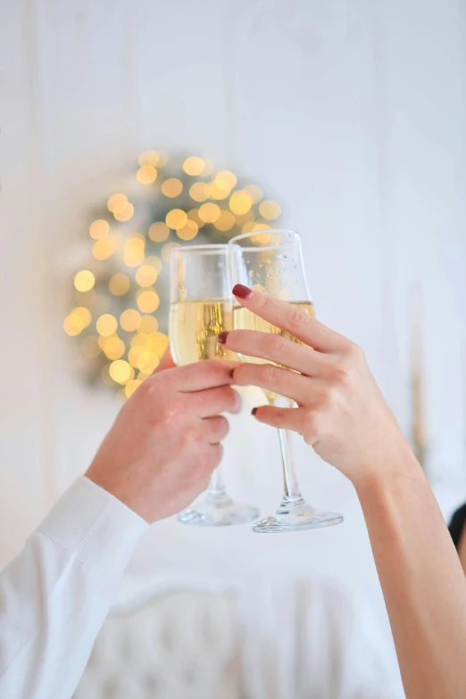 two women toasting wine glasses with white and gold decorations in the background