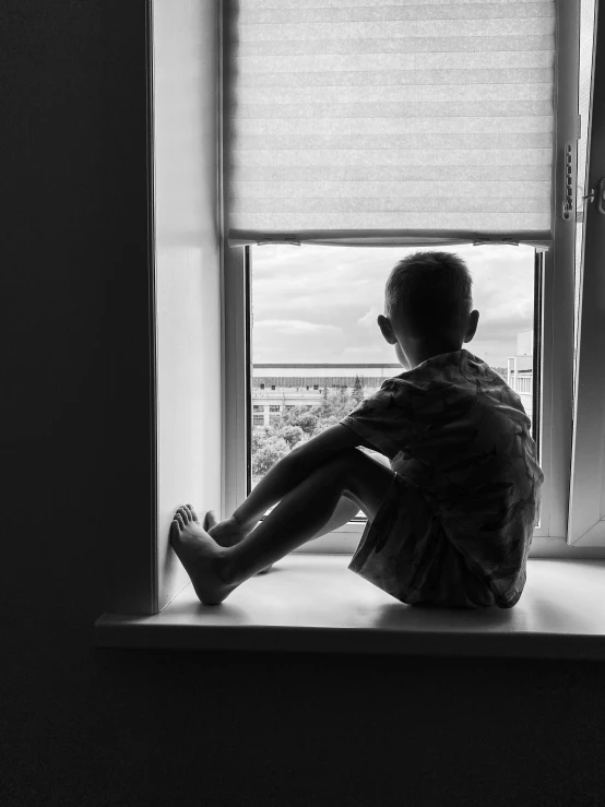 a little boy sitting on a ledge looking out of a window