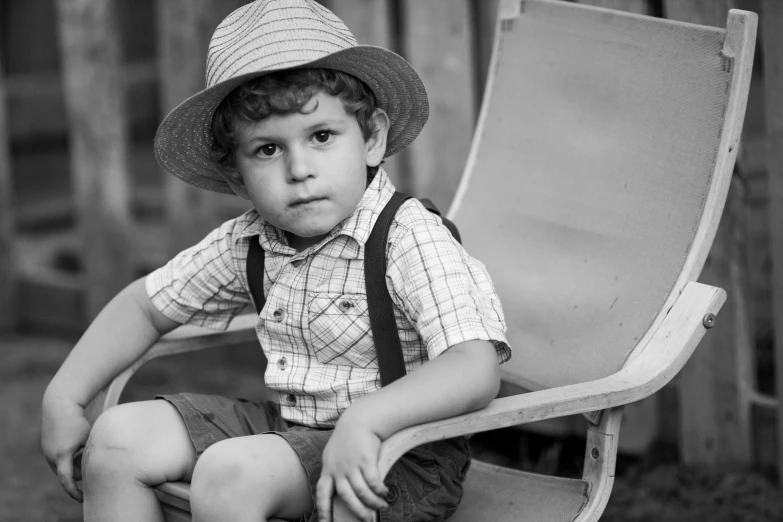 a little boy wearing a hat sitting in a folding chair