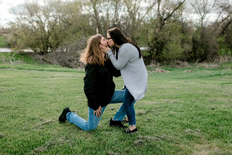 two young women kiss in the middle of a park