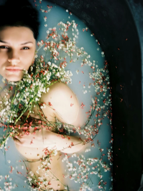 a person lying in a bathtub surrounded by flowers