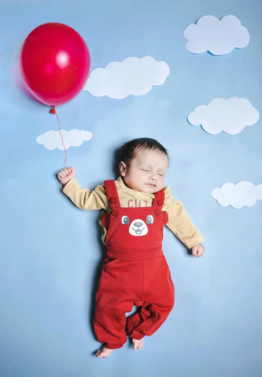 a baby with a balloon and blue wall in the background