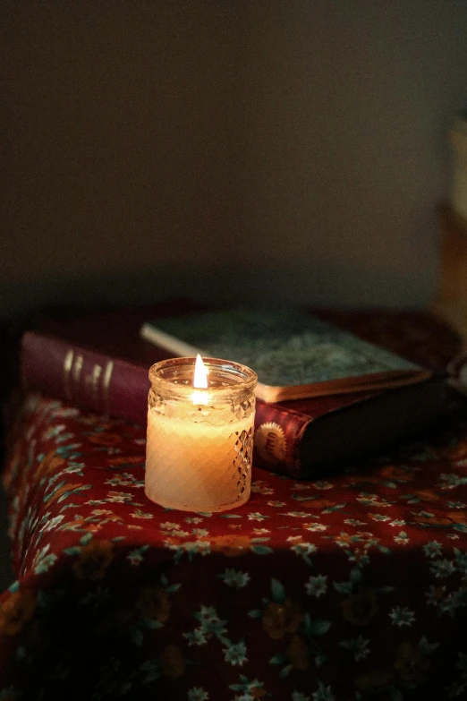 lit candle in small glass jar next to books