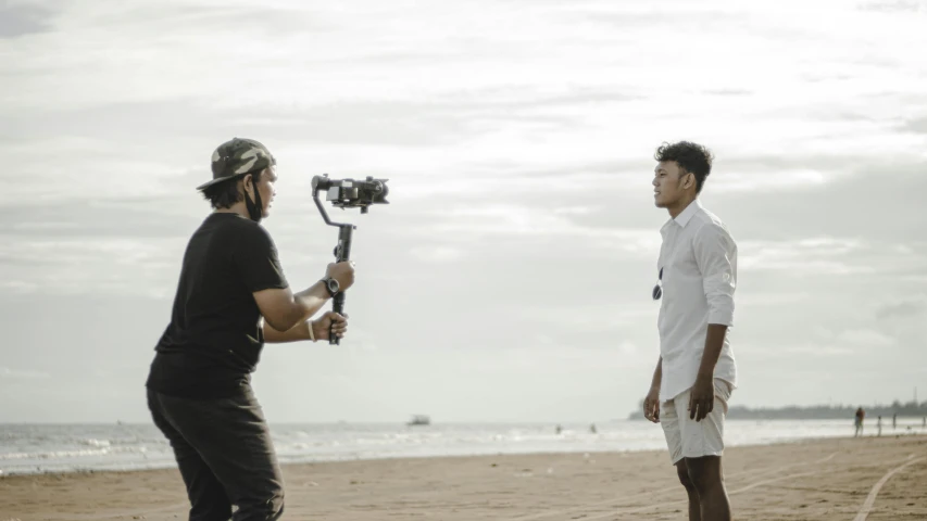 a man standing on a beach next to a person with a camera