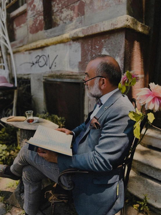 a man reading a book outside with flowers in the background