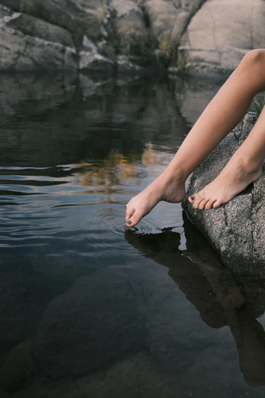 a person's bare toe is standing on a rock by a river