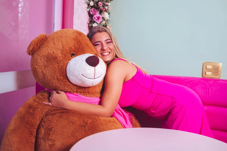 a woman sitting on a pink couch hugging a large teddy bear